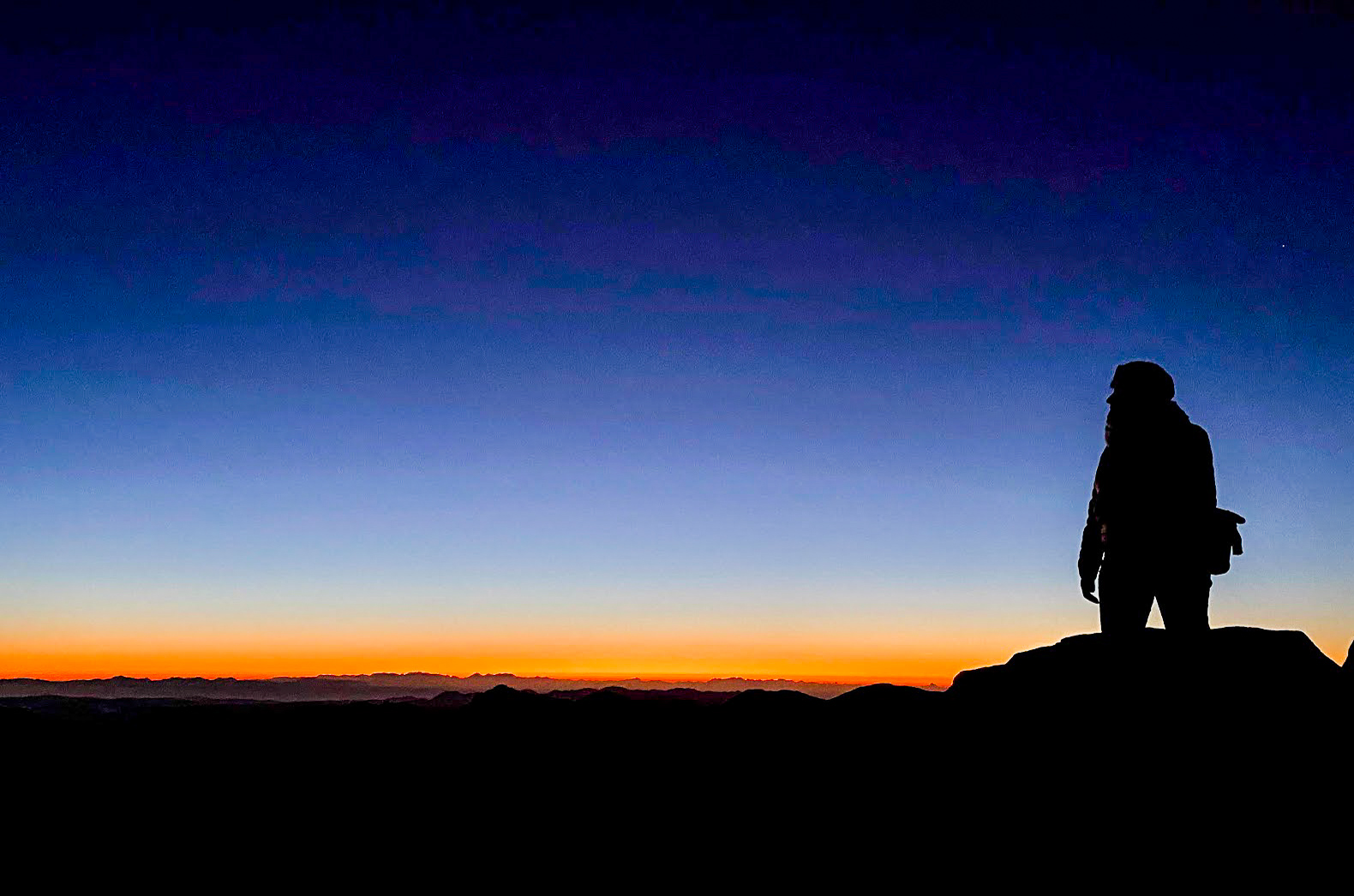 The silhouette of a walker against the sunrise at the summit of Mount Sinai, Egypt