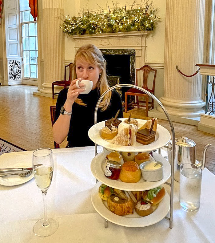 Rosie drinks from a white cup with afternoon tea in the foreground at The Pump Room Bath