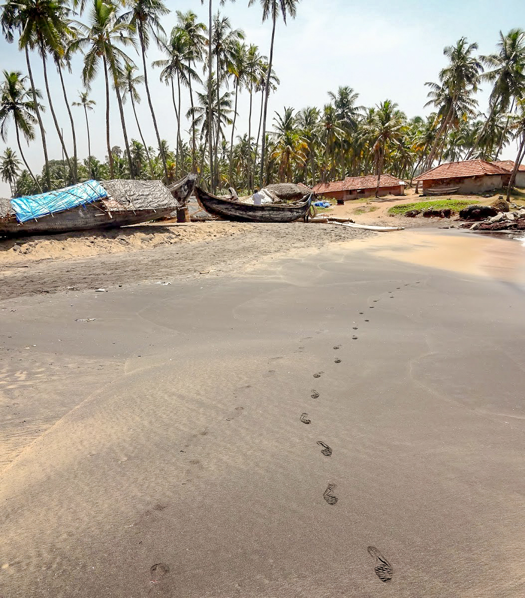 Footprints in the sand on Odayam beach, in the background wooden boats and palm trees, Varkala, Kerala, India