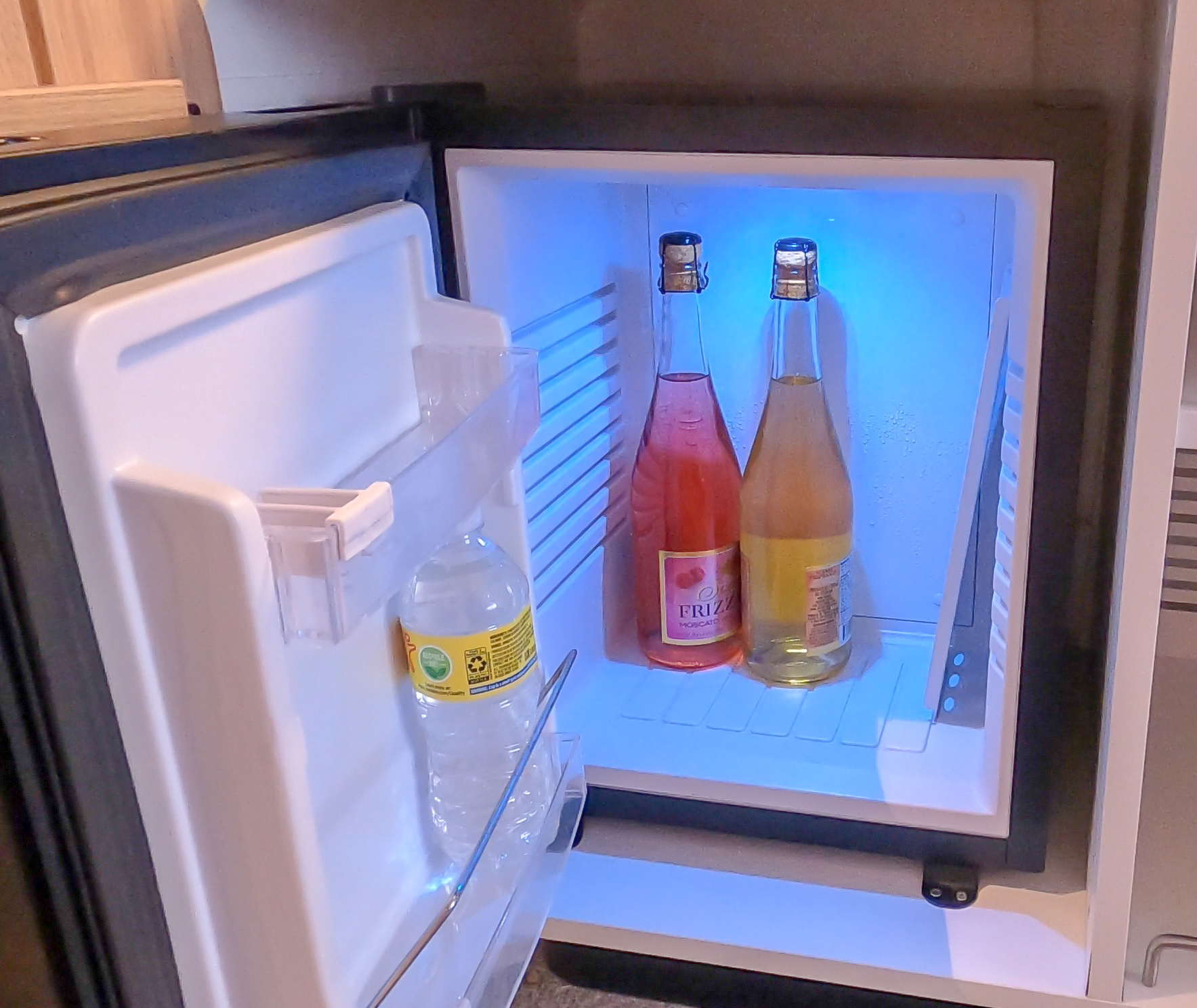 A mini fridge with a bottle of water and 2 bottles of fruity wine